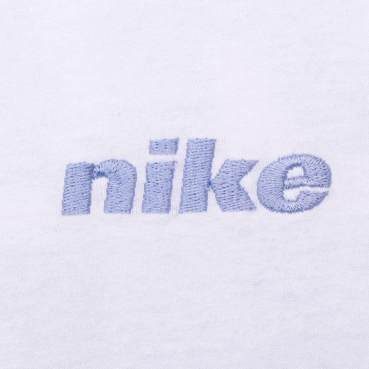 Close-up of light blue embroidered Nike wordmark on white fabric