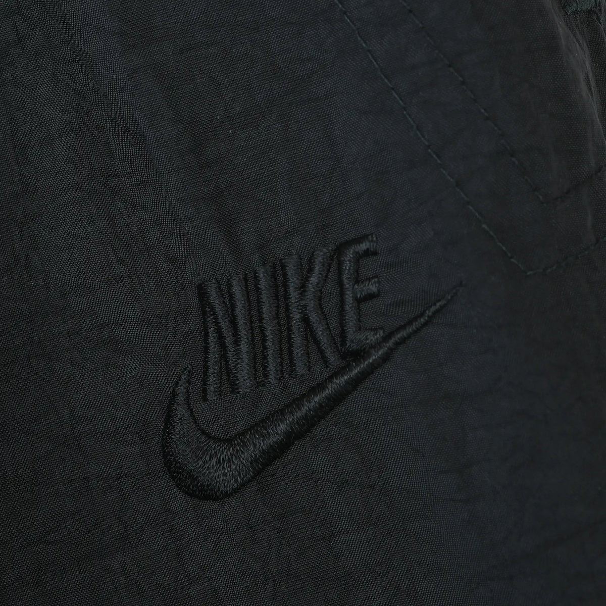 Close-up of tonal black Nike Swoosh embroidery on the track pants