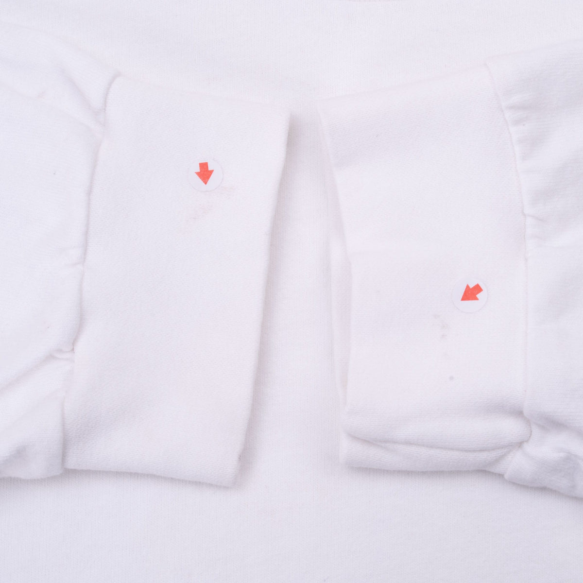 Close-up of white ribbed sleeve cuffs with arrows marking small spots