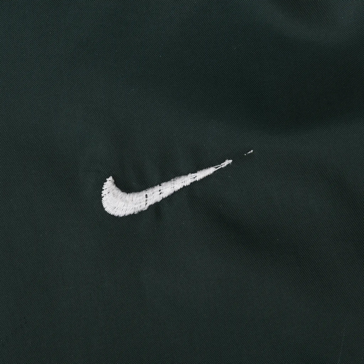 Close-up of white Nike Swoosh embroidery on dark green fabric
