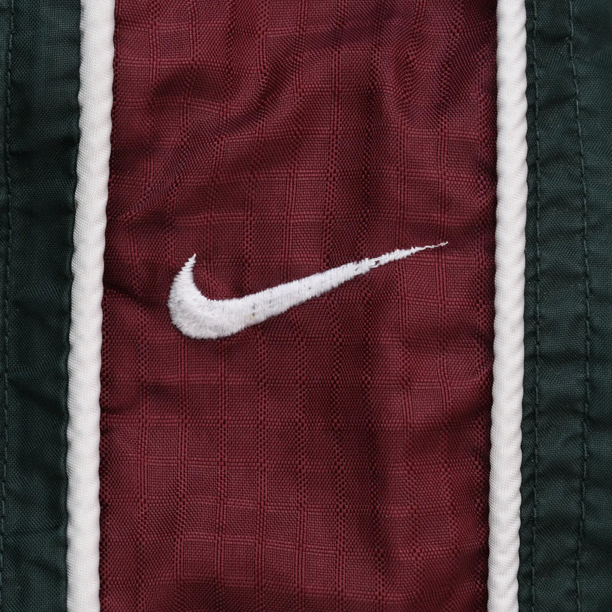 Close-up of white Nike Swoosh embroidery on burgundy side panel with white piping