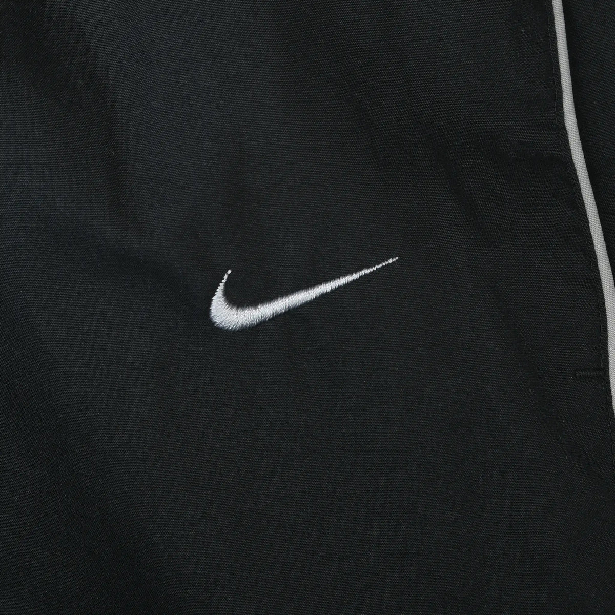 Close-up of white Nike Swoosh embroidery and piping on black track pants