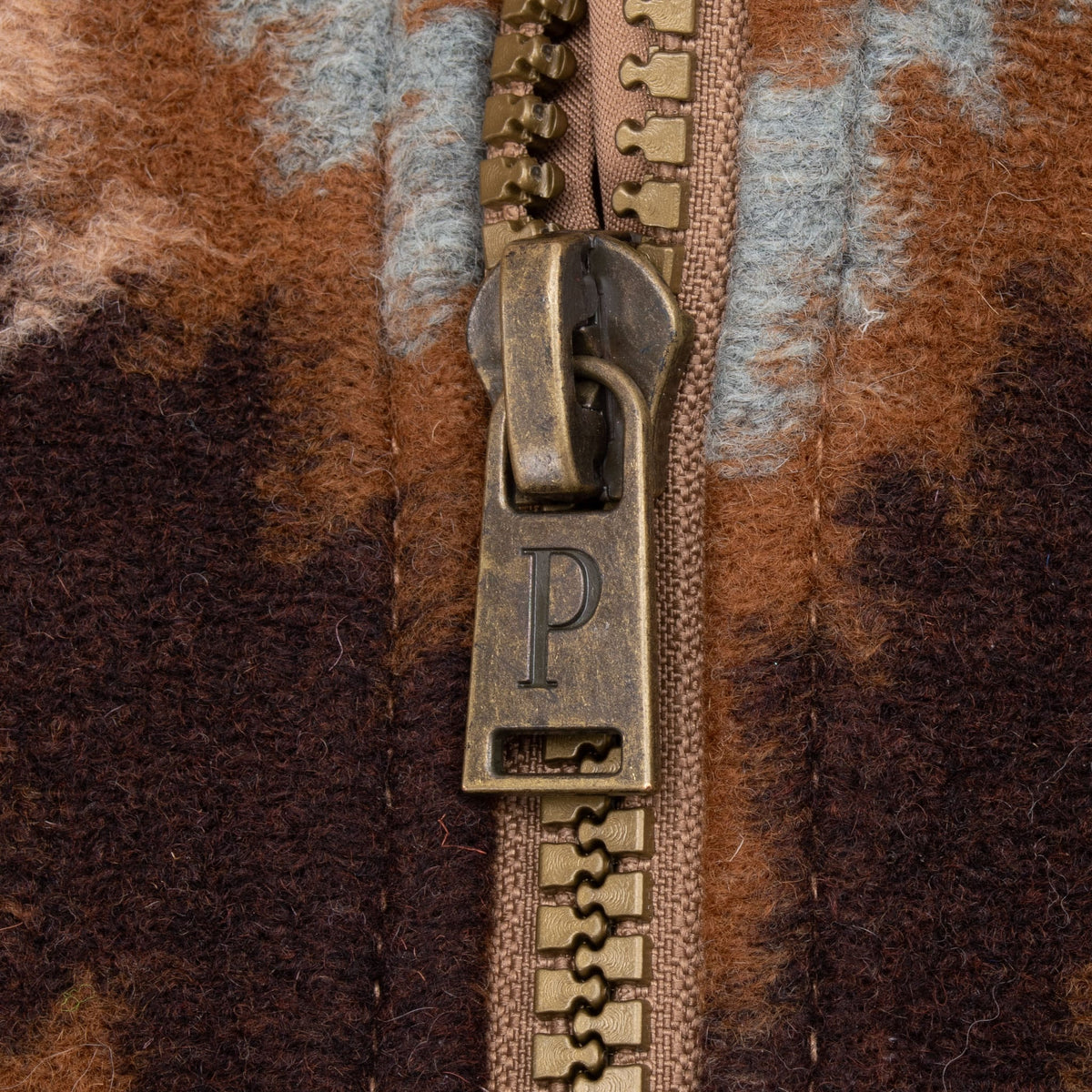 Close-up of antique brass-tone zipper pull embossed with the Pendleton P logo