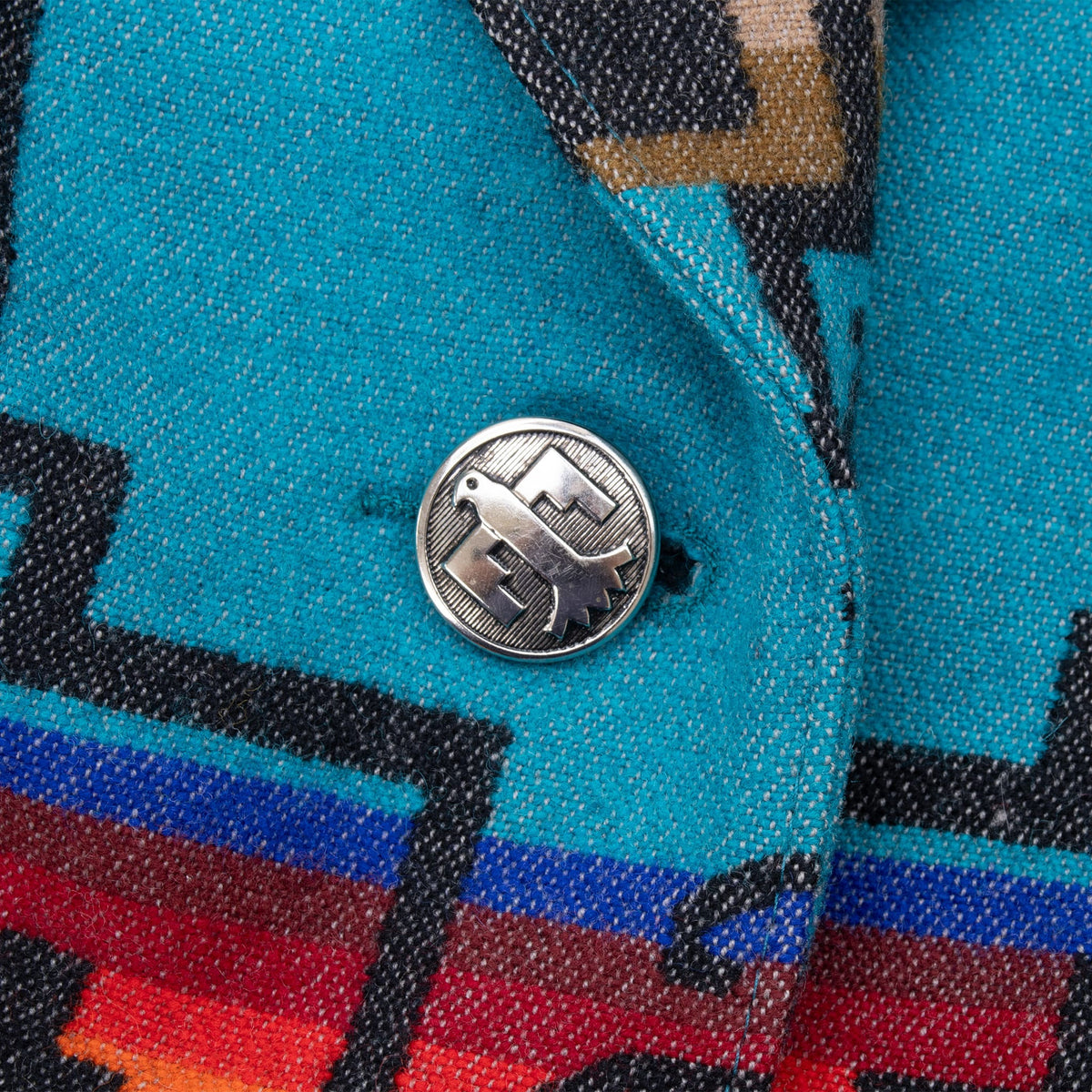 Close-up of decorative silver-tone button on turquoise geometric fabric