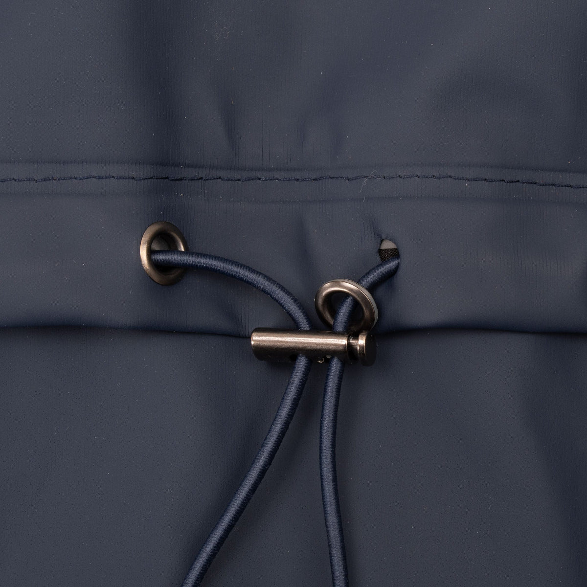 Close-up of back waist drawcord, metal eyelets, and toggle on navy jacket