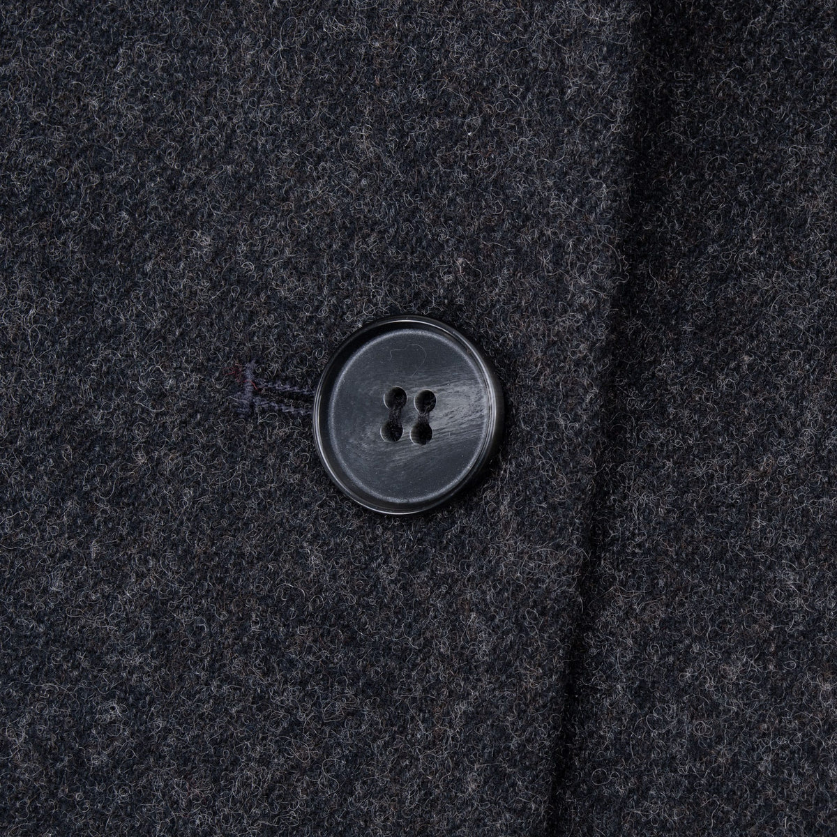 Close-up of black four-hole front button and textured wool blazer fabric