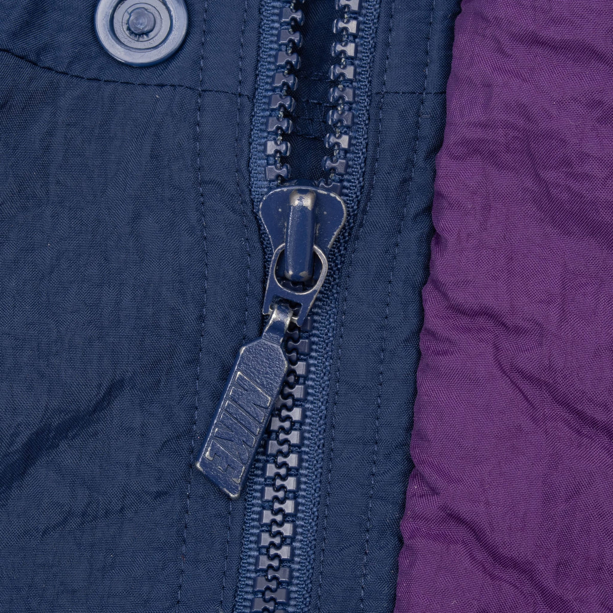 Close-up of Nike-branded zipper pull and snap on blue and purple windbreaker
