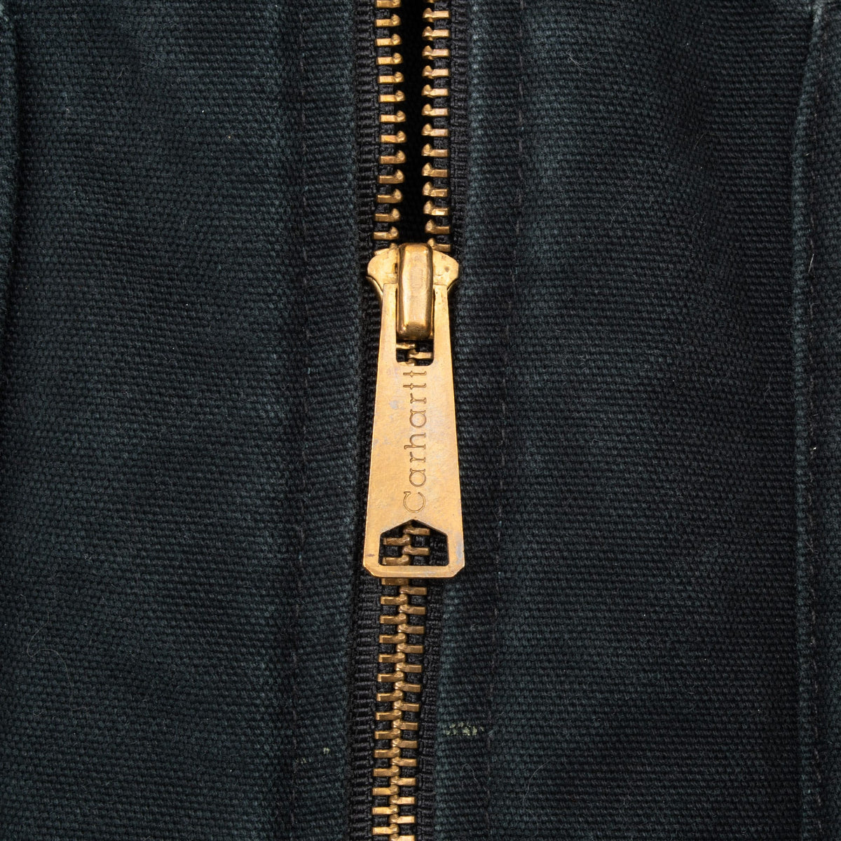 Close-up of brass-tone Carhartt-branded zipper pull on black vest