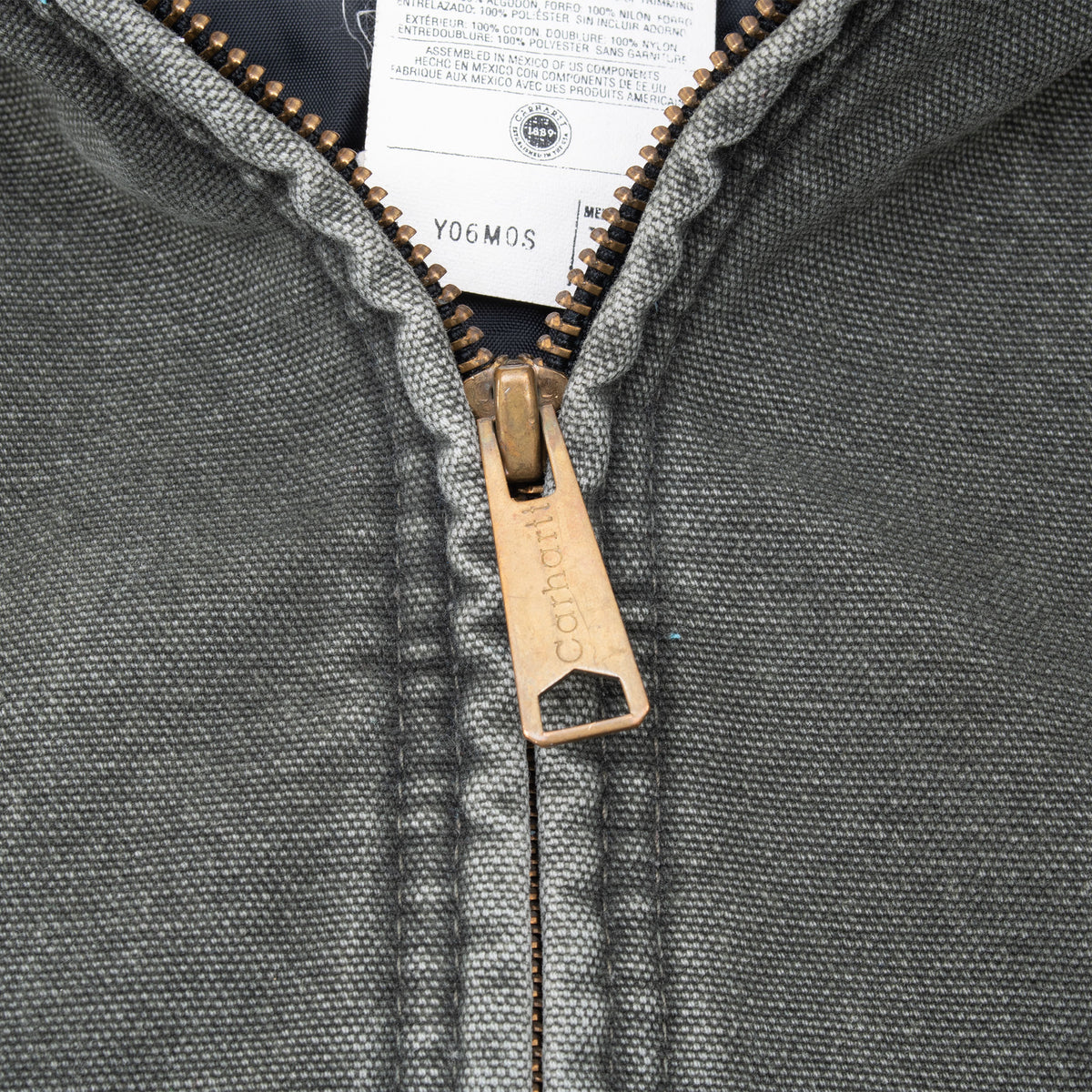 Close-up of Carhartt-branded metal zipper pull on faded green fabric