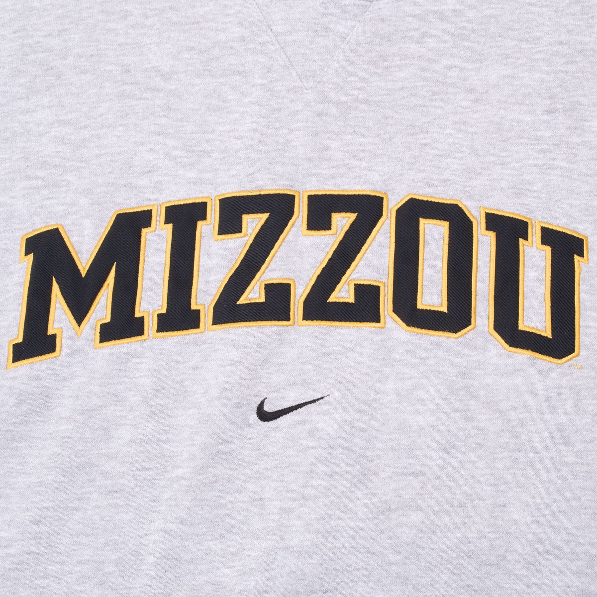 Close-up of black and gold Mizzou lettering and Nike Swoosh on grey sweatshirt