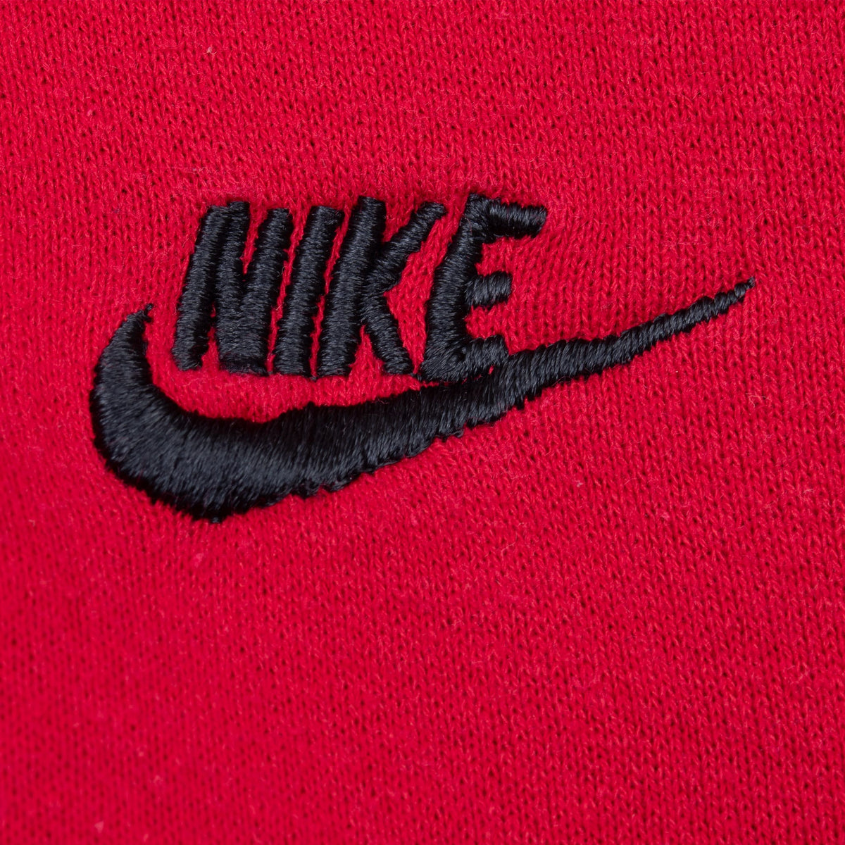 Close-up of black embroidered Nike Swoosh logo on red chest fabric