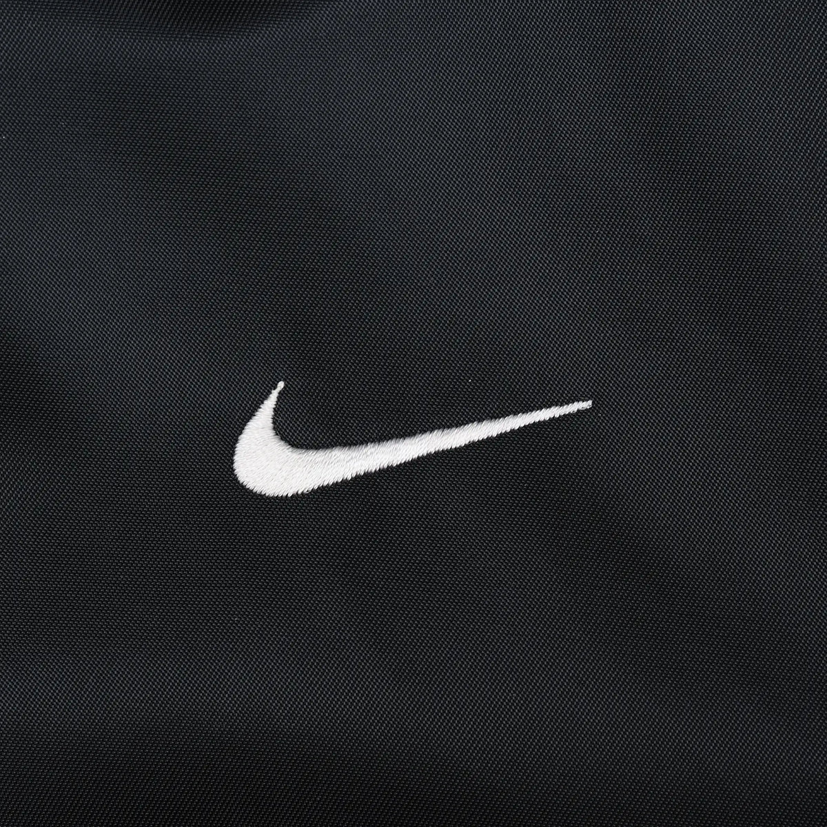 Close-up of small white Nike Swoosh embroidery on black fabric
