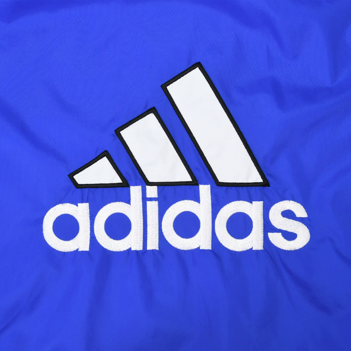 Close-up of large white adidas back logo with black outlines on royal blue fabric