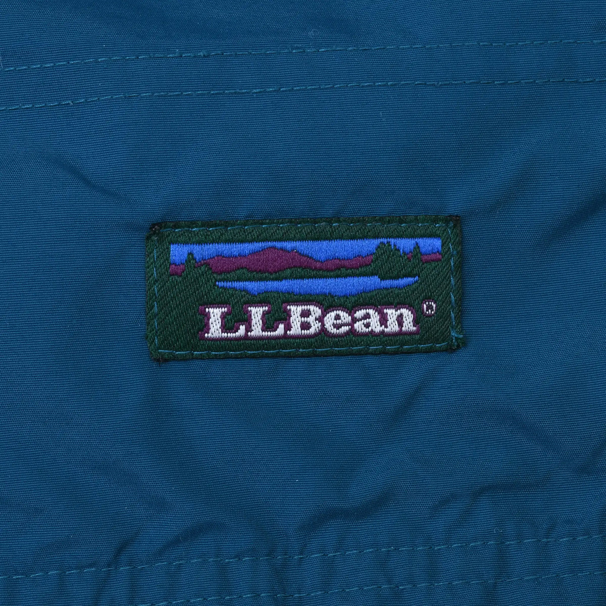 Close-up of embroidered L.L.Bean landscape logo patch on teal fabric