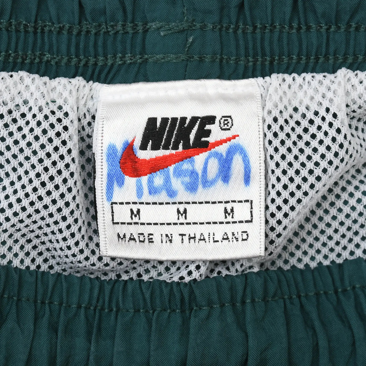 Nike size medium label inside green swim trunks above white mesh lining