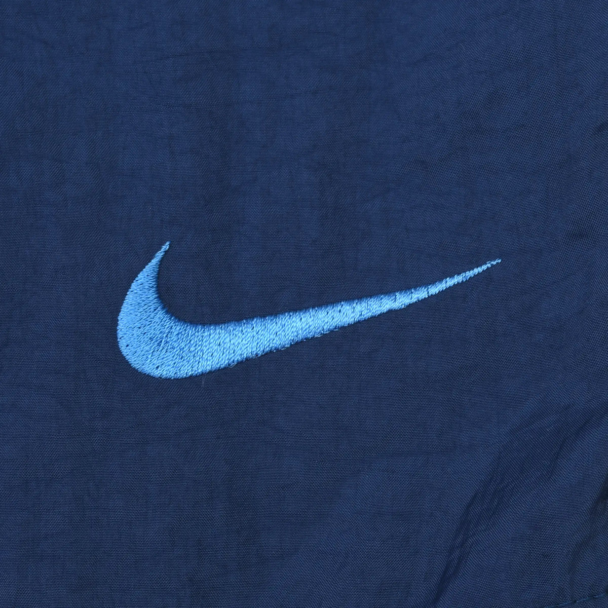 Close-up of small light blue embroidered Nike Swoosh on navy fabric