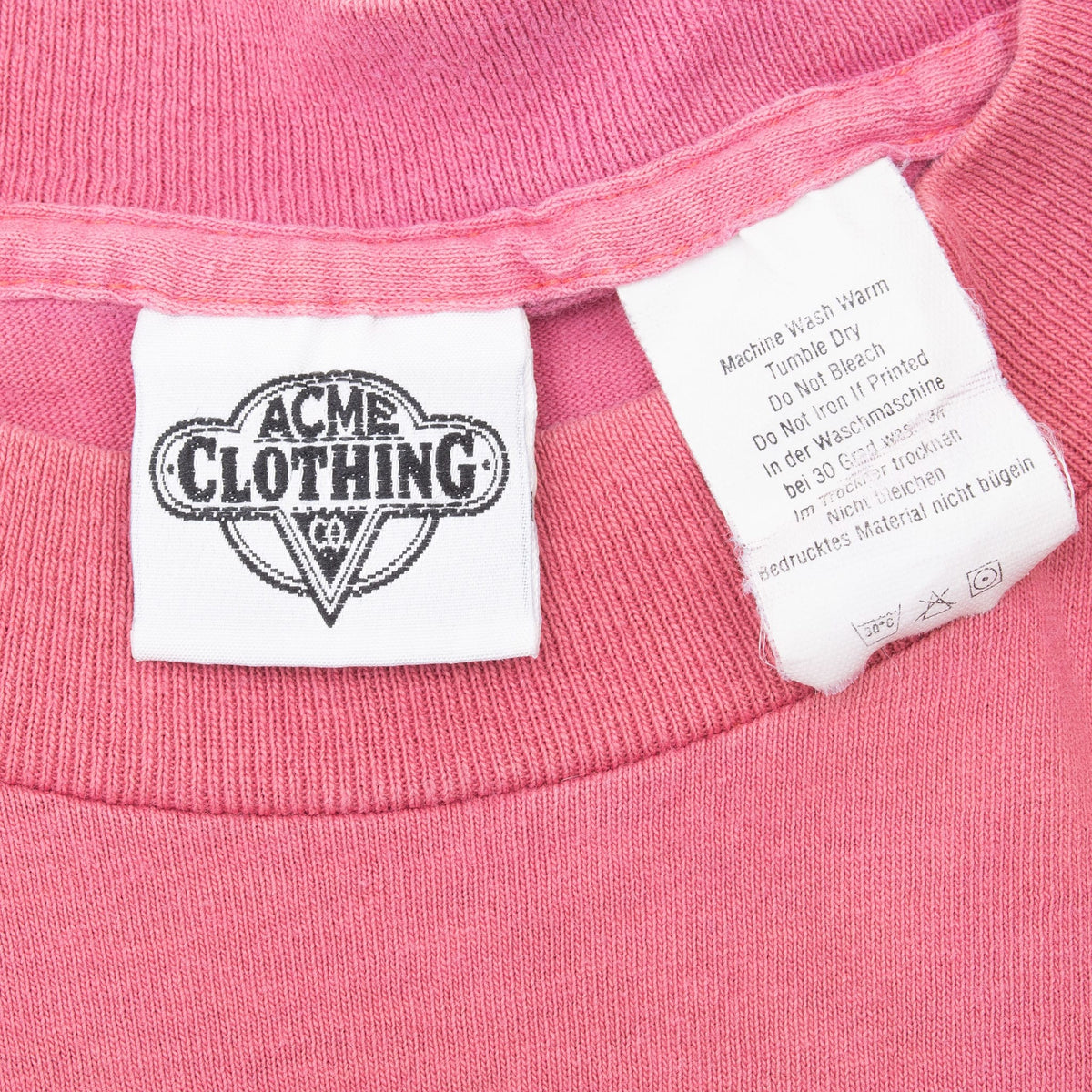Close-up of ACME Clothing neck label and care tag inside pink T-shirt