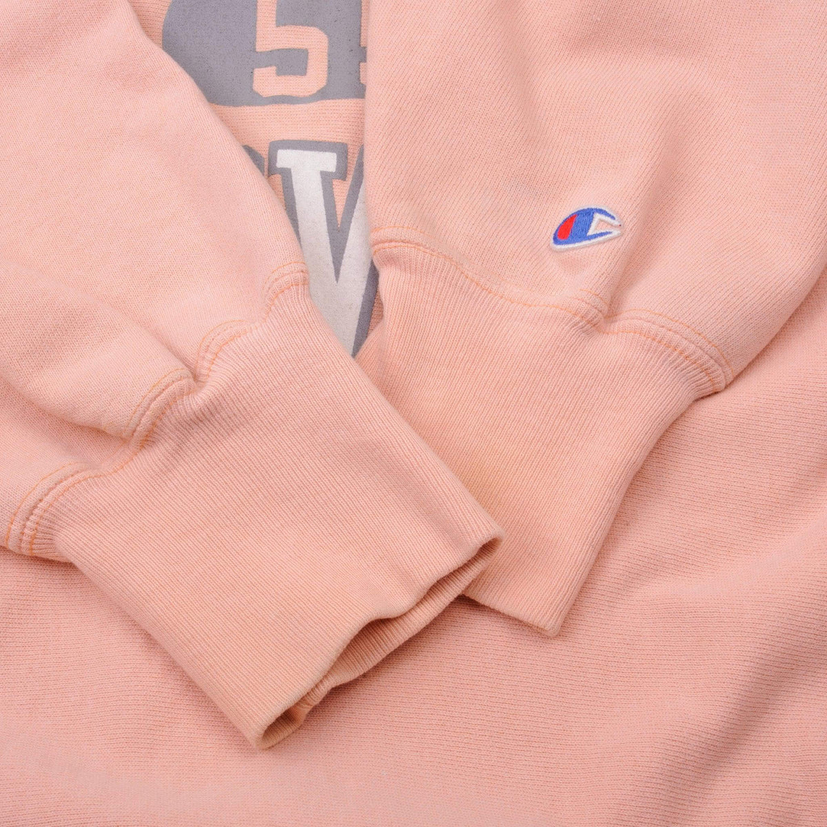 Close-up of ribbed cuffs and embroidered Champion sleeve logo on pink sweatshirt