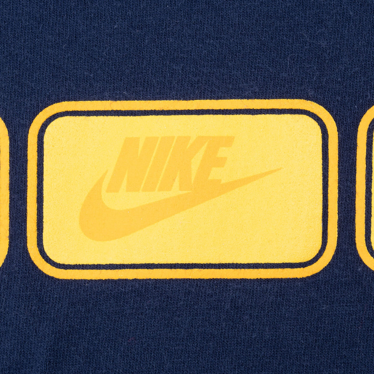 Close-up of yellow Nike wordmark and Swoosh chest print on navy fabric