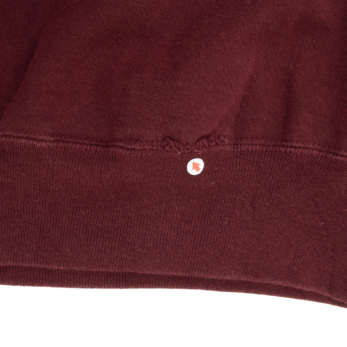 Close-up of small tear along the burgundy sweatshirt's ribbed bottom hem seam
