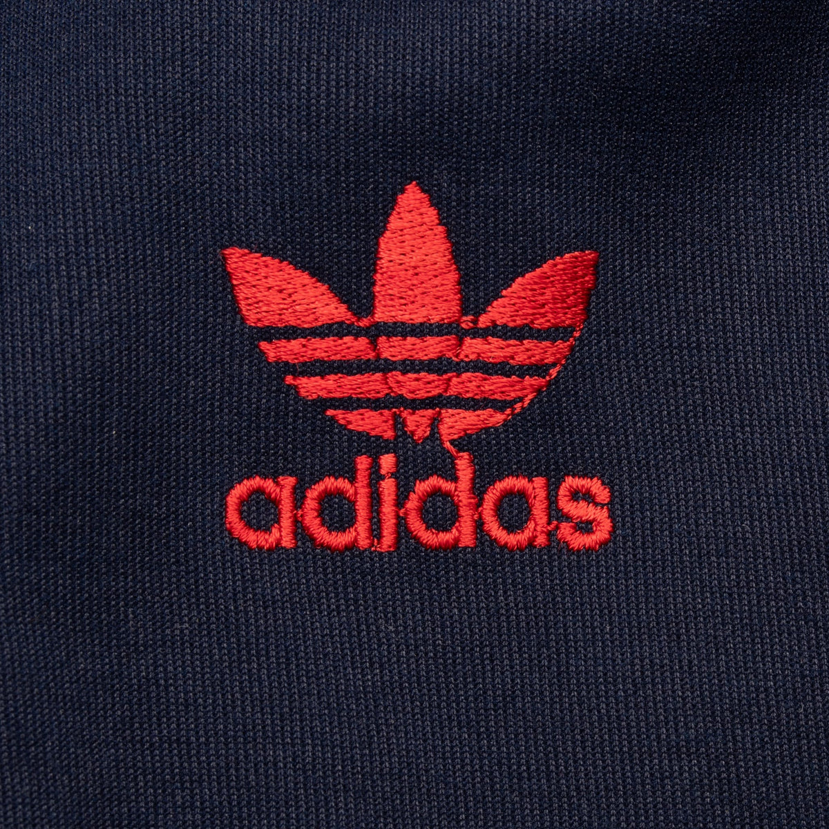 Close-up of red embroidered adidas Trefoil chest logo on navy fabric