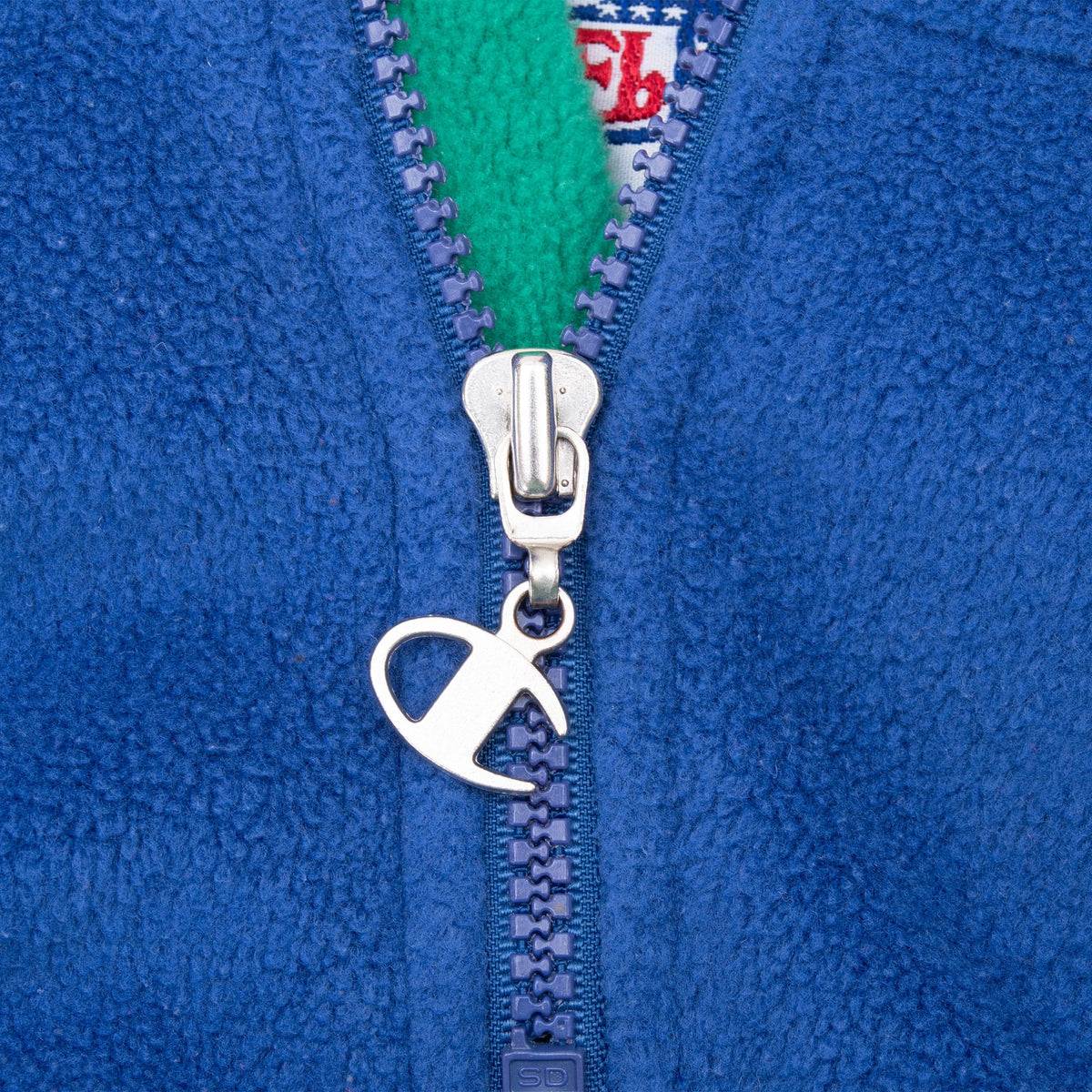 Close-up of Champion logo zipper pull and green collar lining on blue fleece