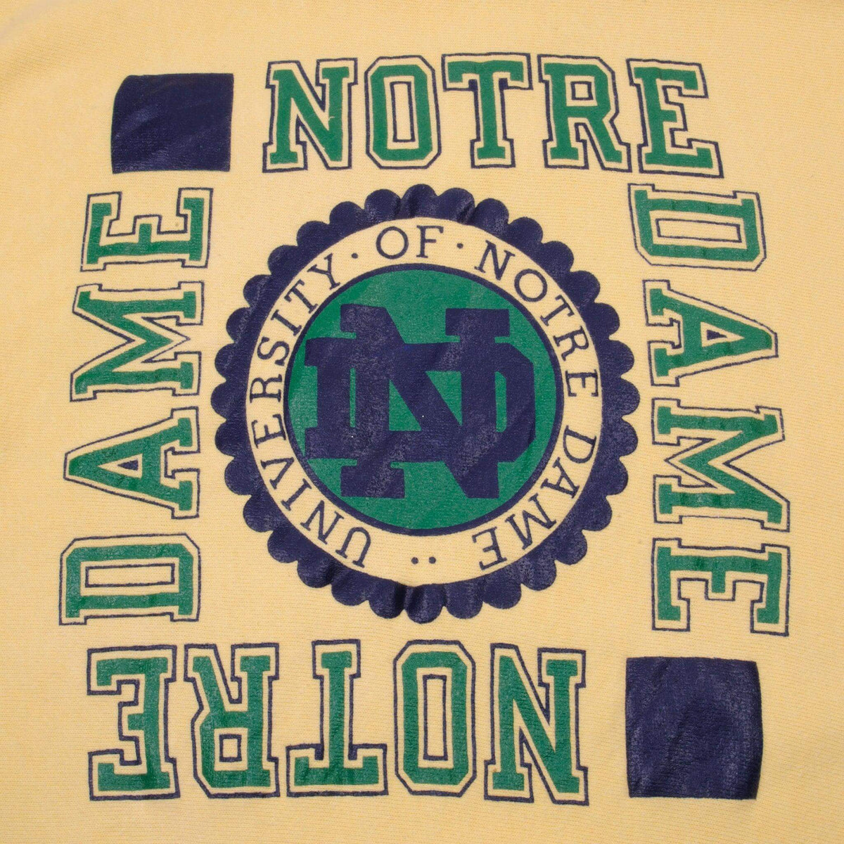 Close-up of green and navy Notre Dame crest print on yellow sweatshirt
