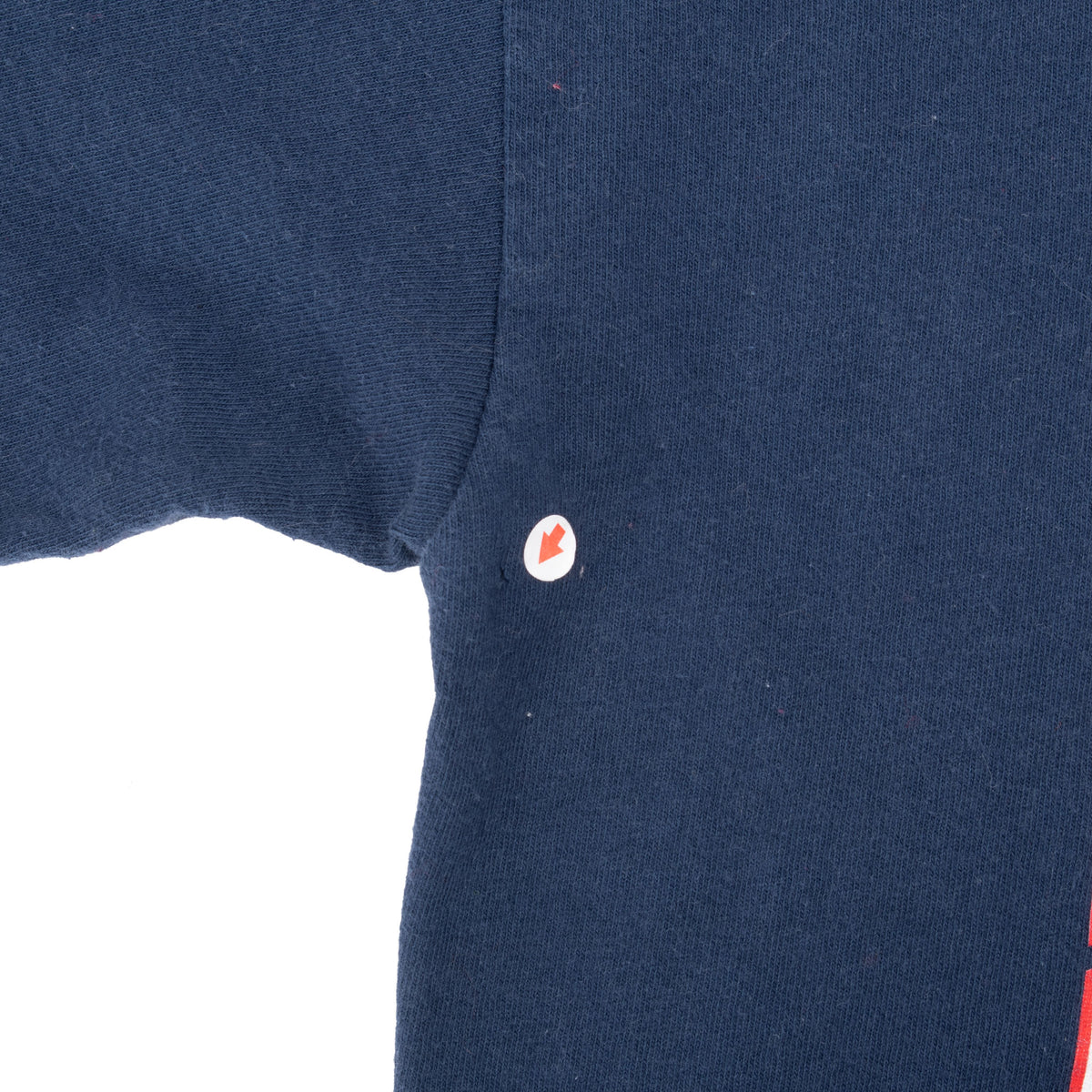 Navy T-shirt underarm detail with small circular red-and-white mark