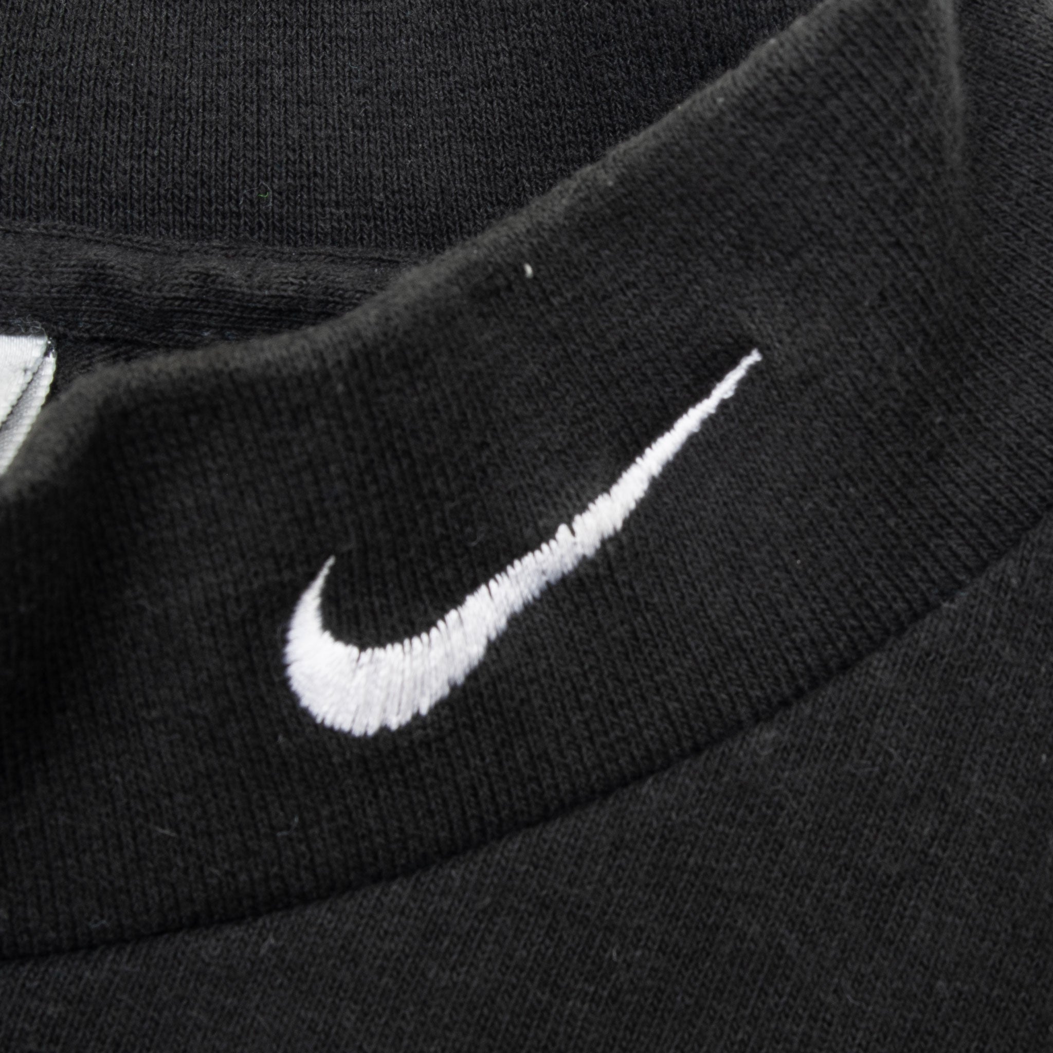 Close-up of white embroidered Nike Swoosh on black ribbed turtleneck collar