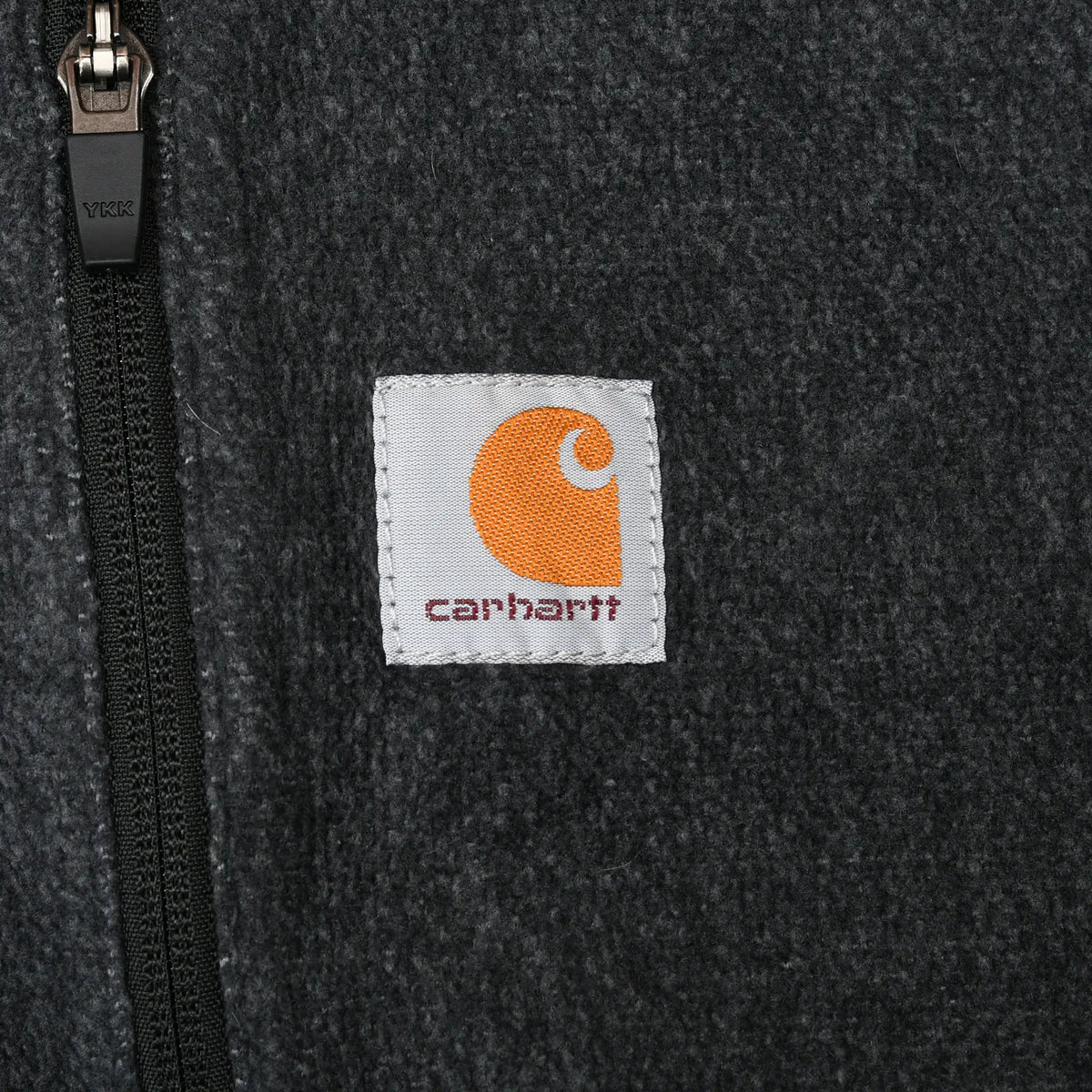 Close-up of Carhartt logo patch beside the chest pocket zipper on dark grey fleece