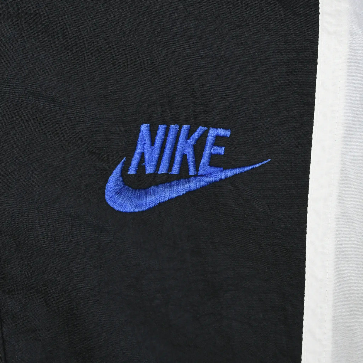Close-up of blue Nike Swoosh embroidery on the windbreaker's black chest panel