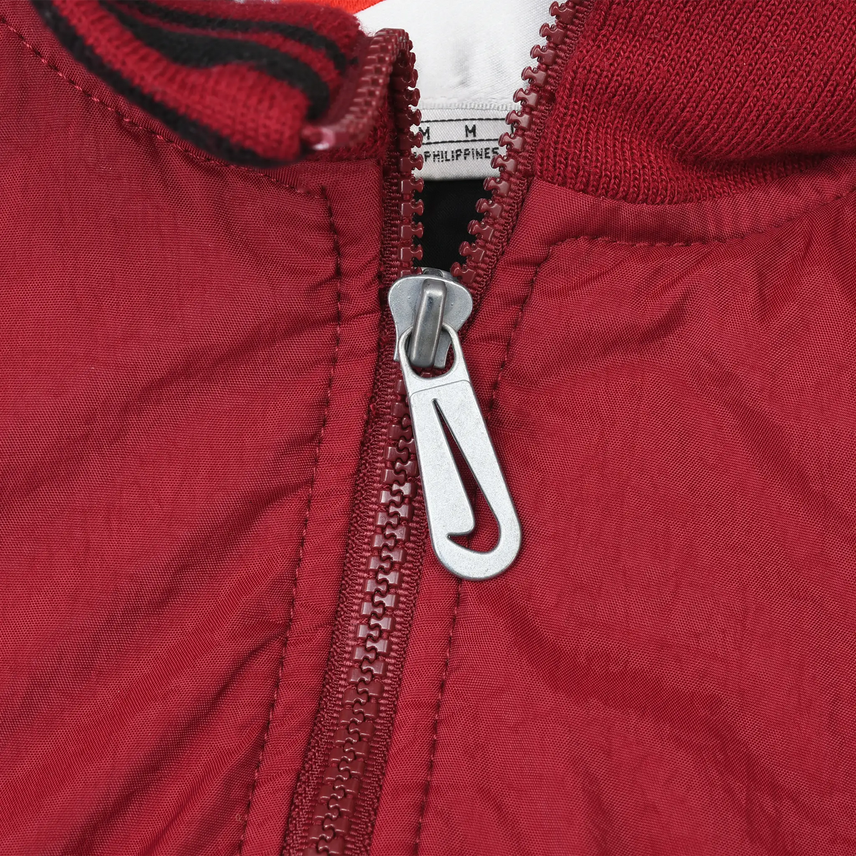 Close-up of burgundy half zipper with silver Nike Swoosh pull and striped collar