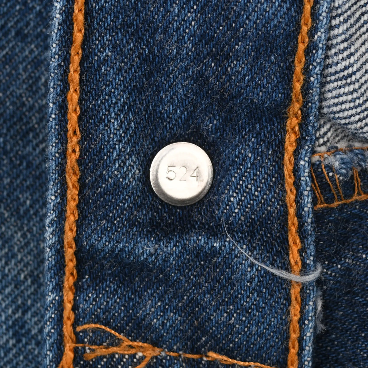 Close-up of Levi's jeans button back stamped 524 beside orange stitching
