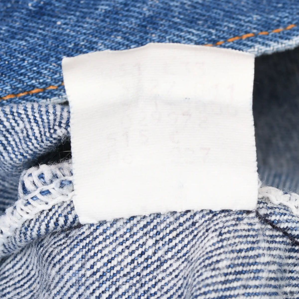 Reverse side of faded white interior label against blue denim seams