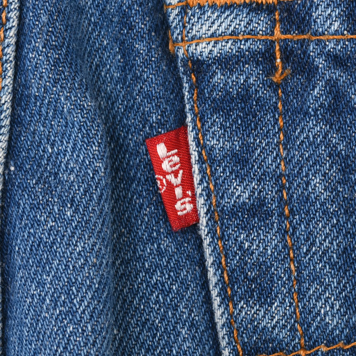 Red Levi's tab beside orange-stitched back pocket on blue denim