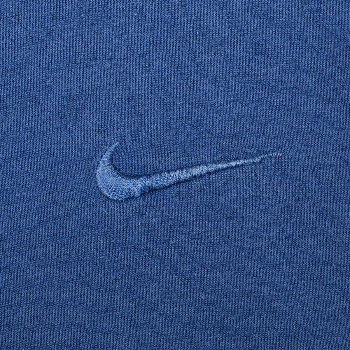 Close-up of tonal blue Nike Swoosh embroidery on T-shirt chest