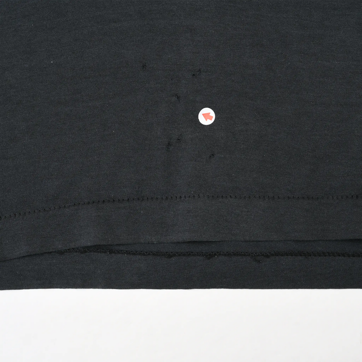 Close-up of black fabric near the bottom hem with a small flaw marked by an arrow