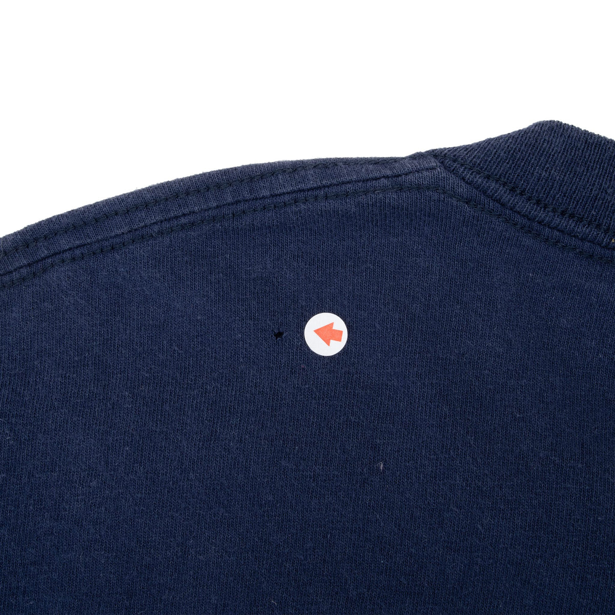 Upper back detail of navy T-shirt with arrow marking a small hole near the shoulder