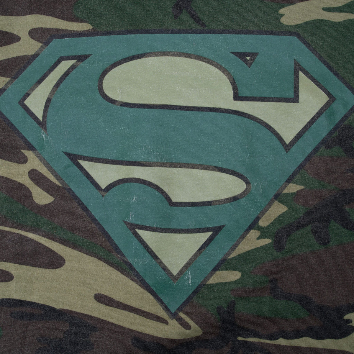 Close-up of teal and tan Superman shield graphic on camouflage print
