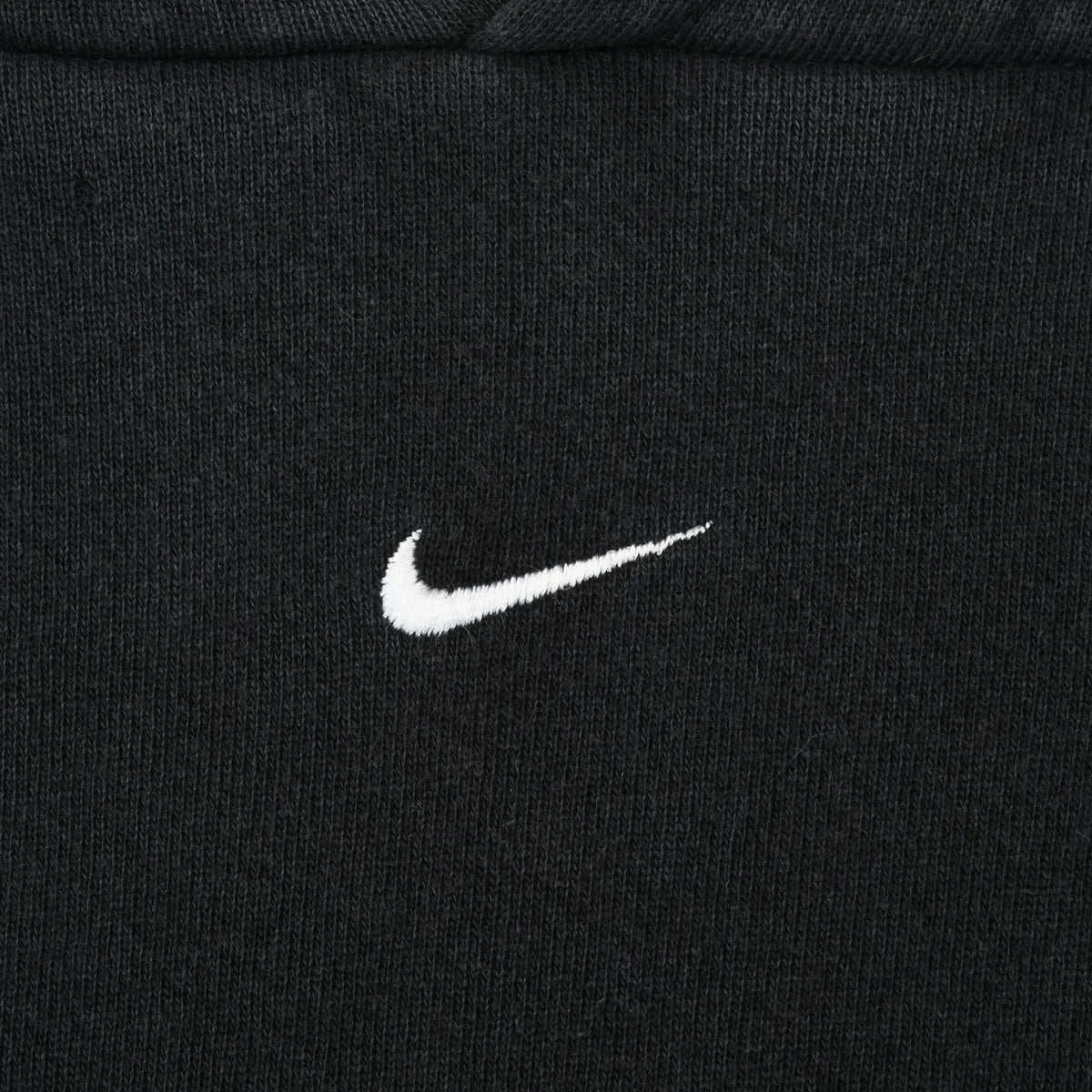 Close-up of small white Nike Swoosh embroidery centered on black chest fabric