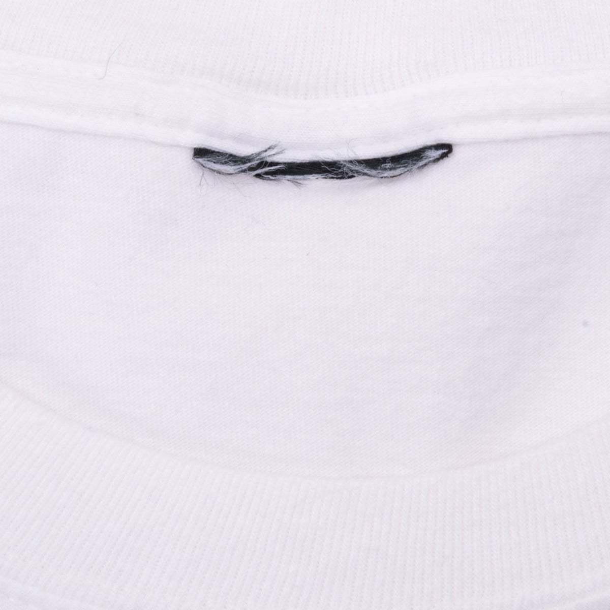 Inside collar detail of white T-shirt showing cut neck label and loose black threads