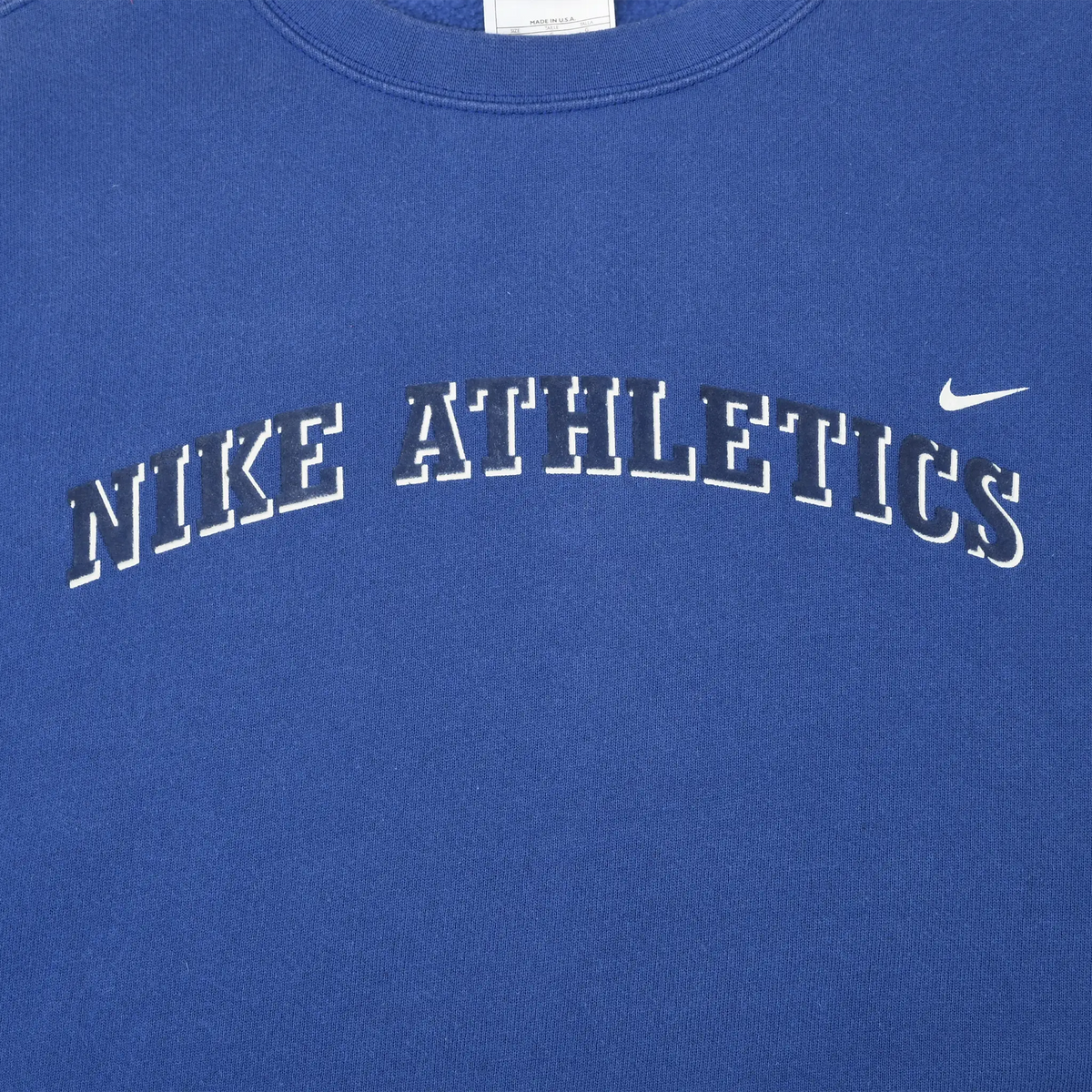 Close-up of arched Nike Athletics chest lettering and white Swoosh on blue sweatshirt