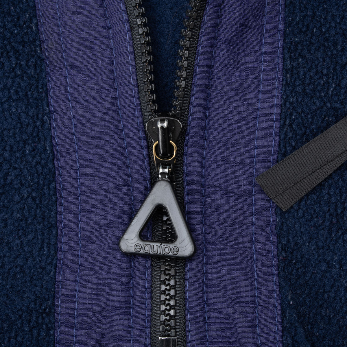 Close-up of Equipe triangle zipper pull and purple placket on navy fleece