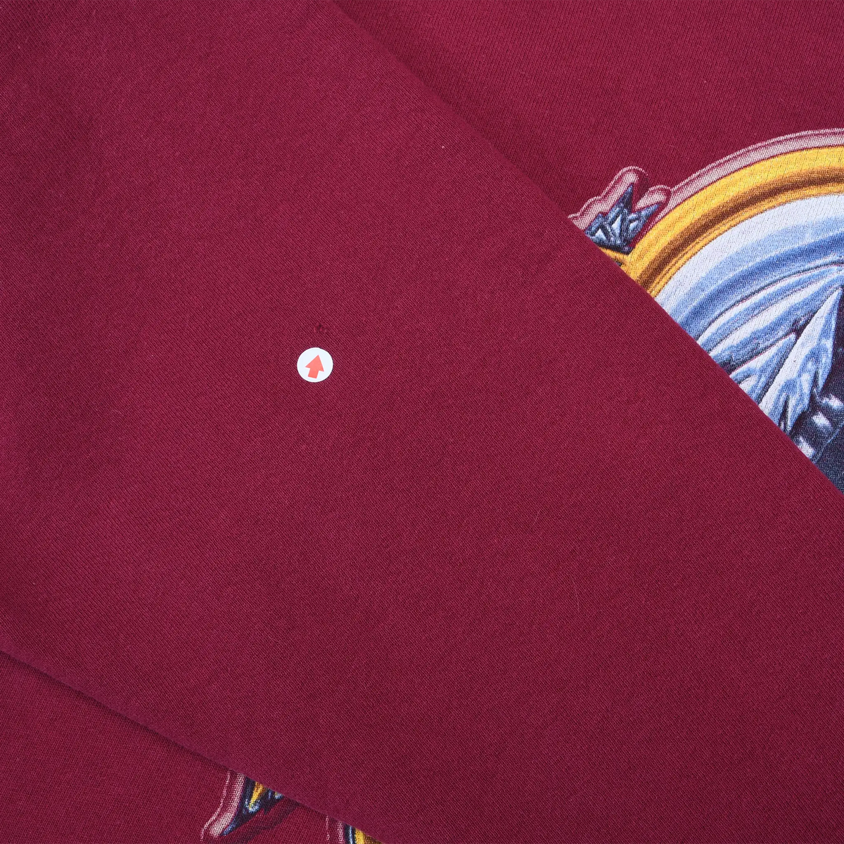 Close-up of small white spot on burgundy sweatshirt sleeve beside part of the chest graphic
