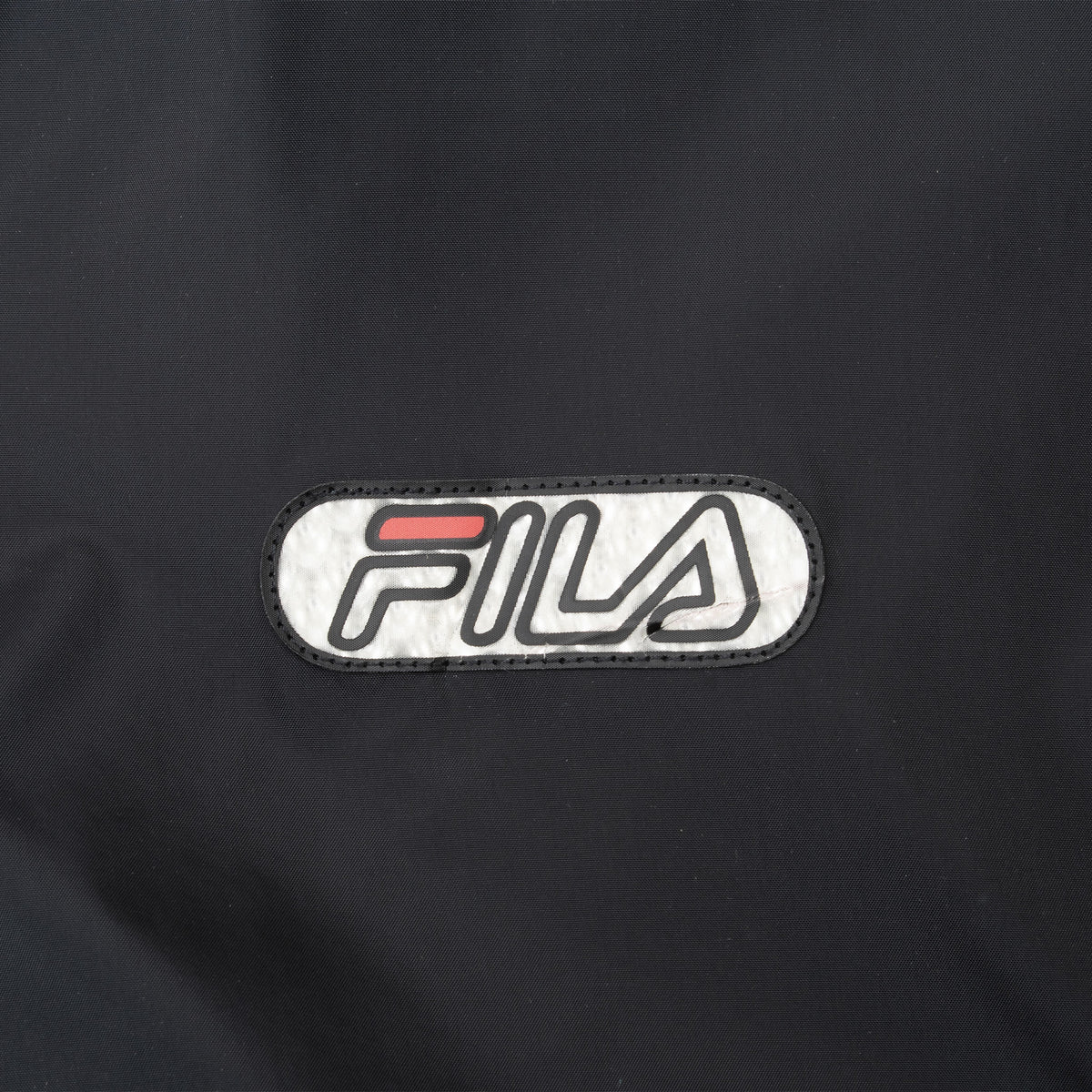 Close-up of Fila logo patch on black windbreaker chest
