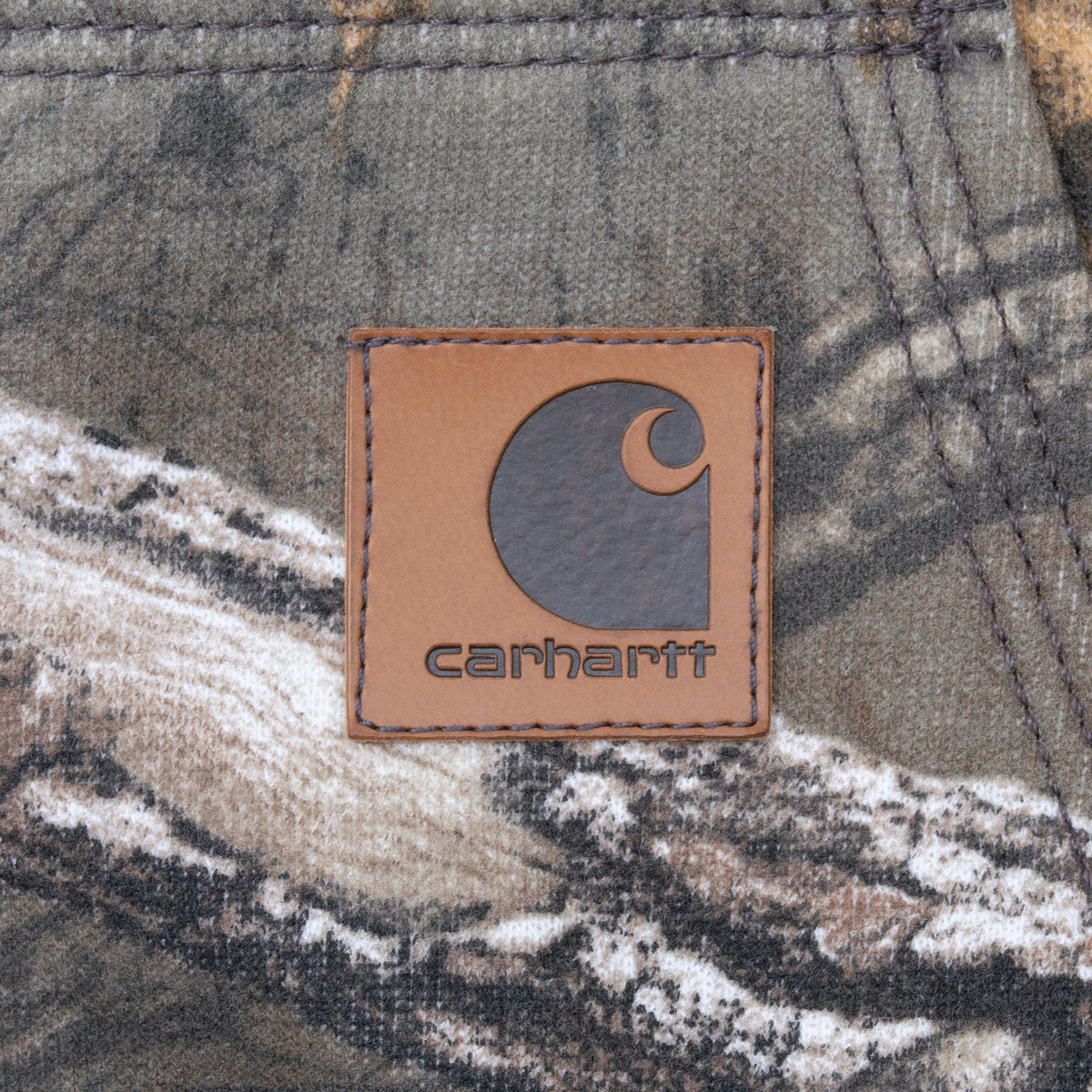 Close-up of brown Carhartt logo patch stitched to the camouflage front pocket