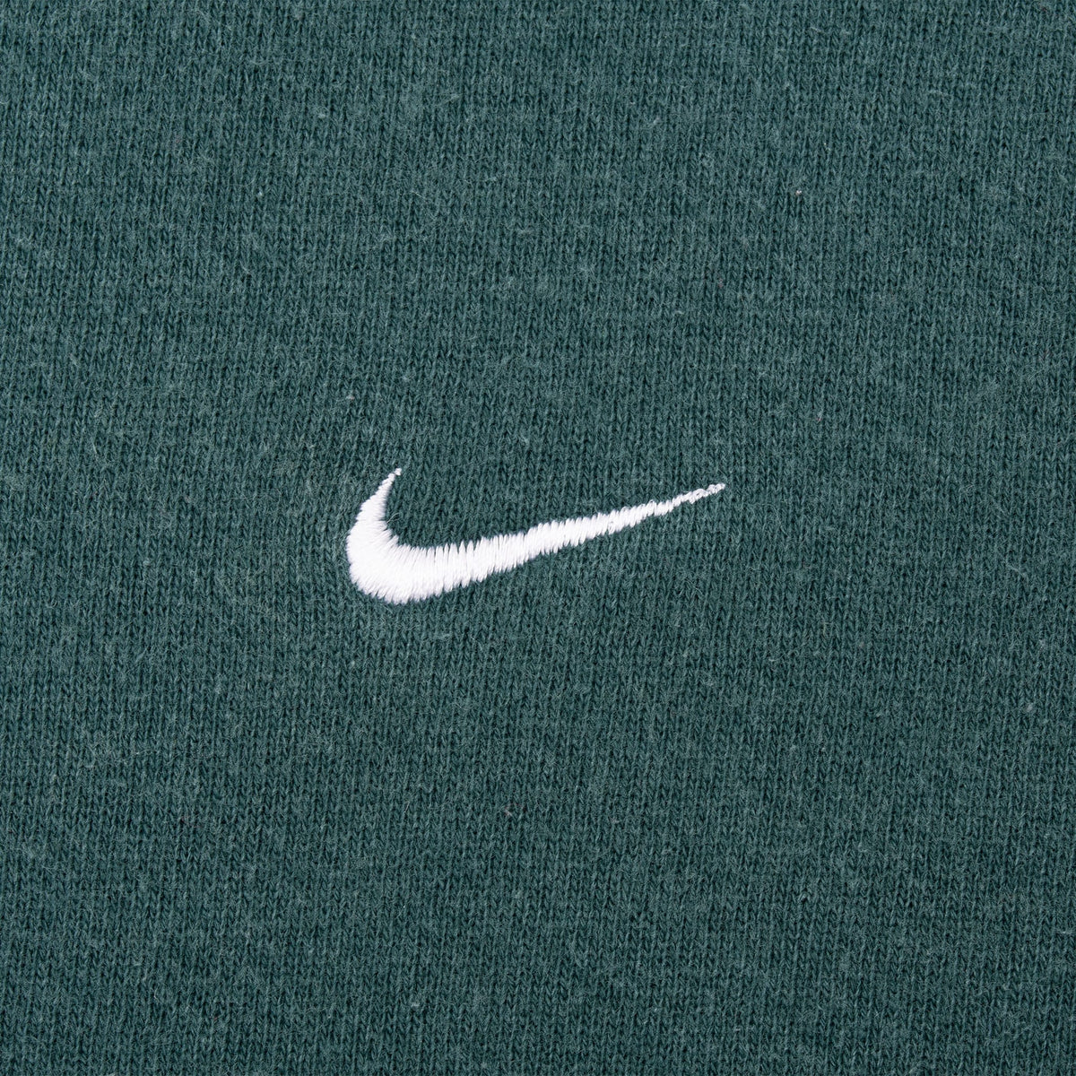 Close-up of white embroidered Nike Swoosh on green sweatshirt chest