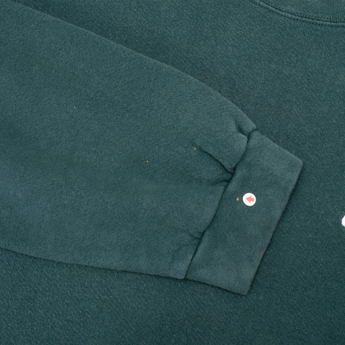 Close-up of green sweatshirt sleeve and ribbed cuff with a small spot marked by an arrow