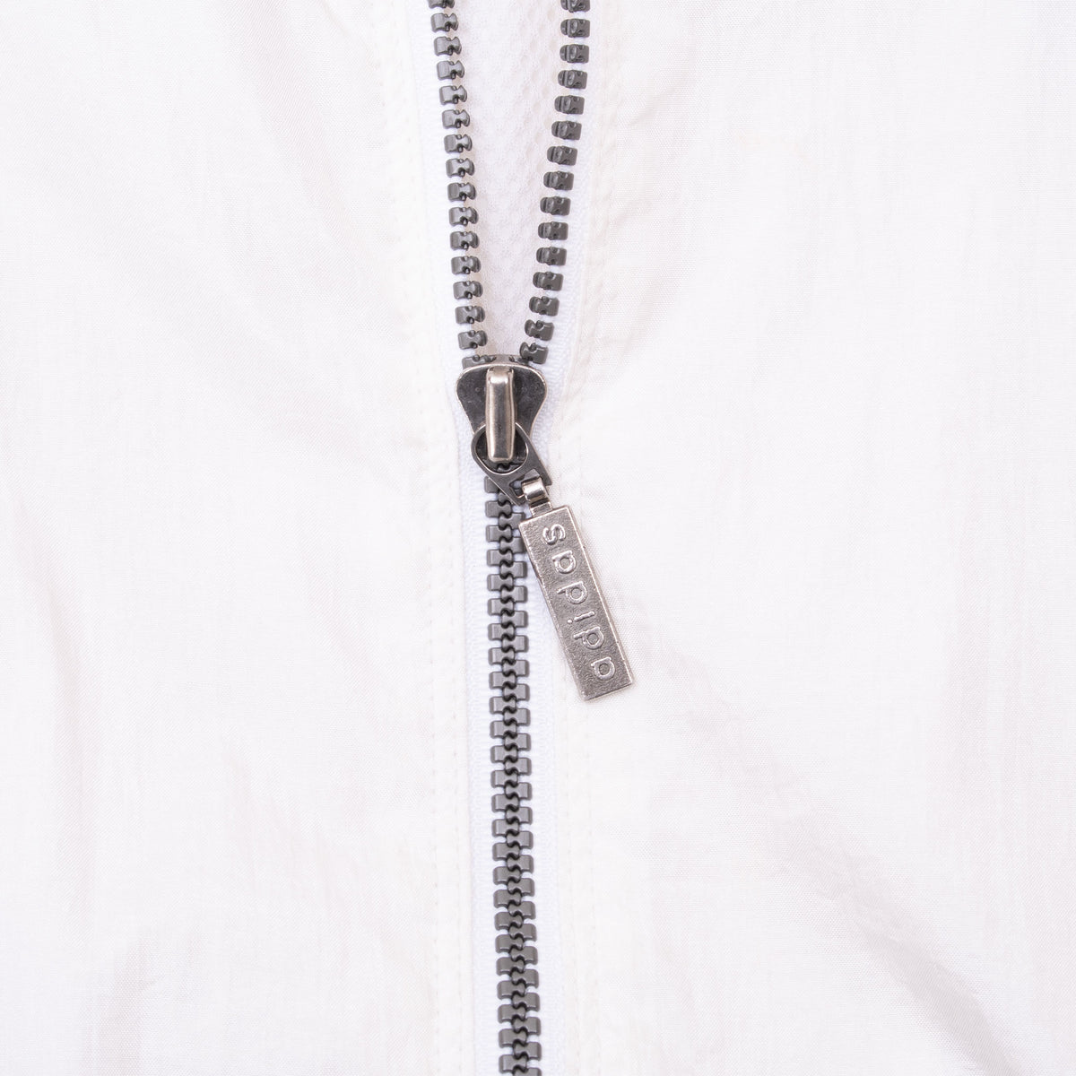 Close-up of metal Adidas zipper pull and black zipper on white fabric
