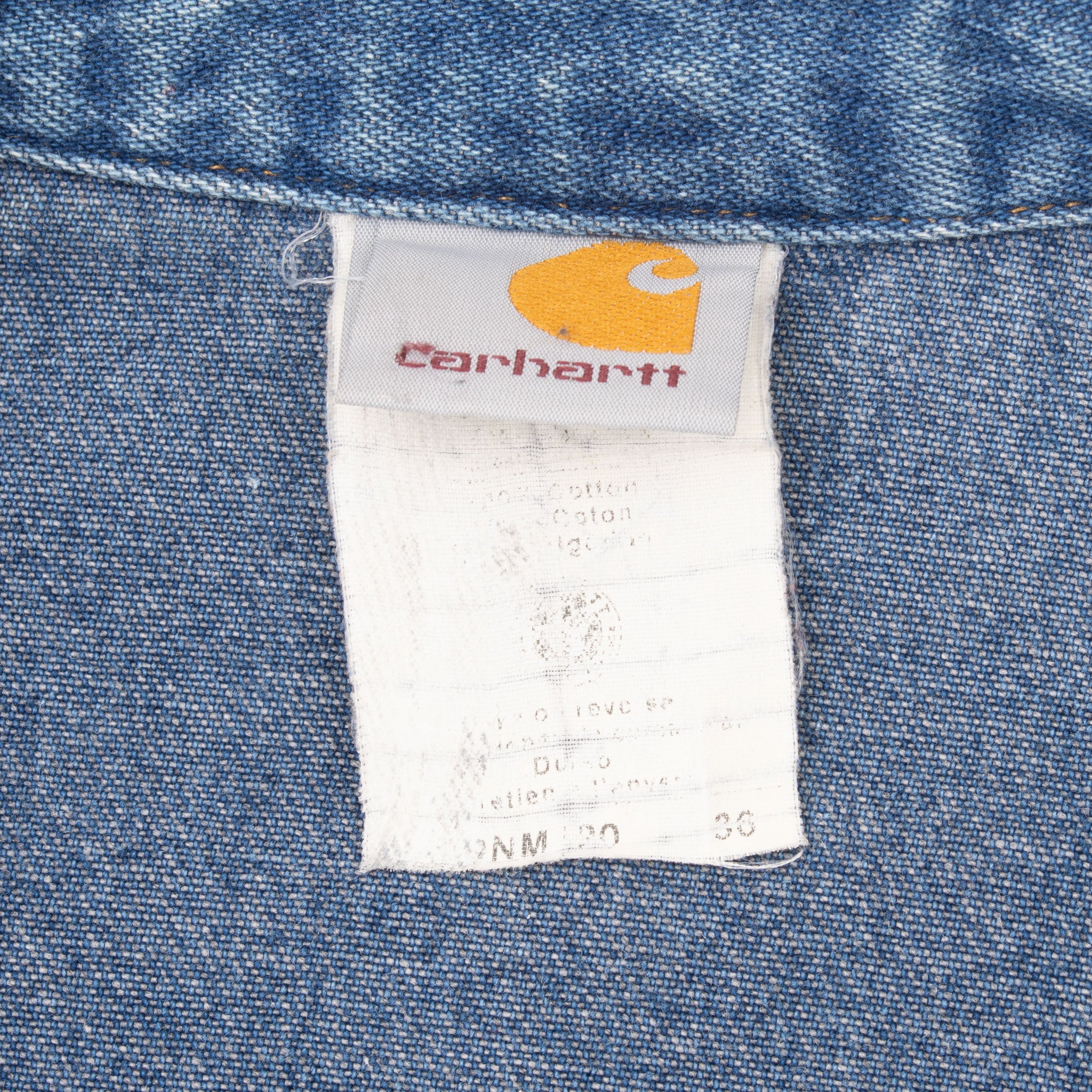Close-up of Carhartt neck label and faded care tag inside blue denim shirt